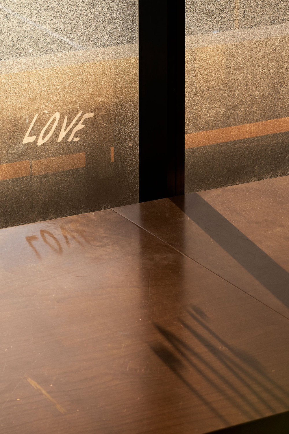 A photo of a window in the Cool Change office. A sticker is stuck to the screen, depicting the letters "L, O, V, E". The light, pouring through the window casts shadows of the letters onto the desk in front of it.