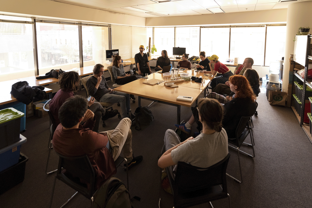A wide angle photo of a group of people seated around a desk in the Cool Change Office.